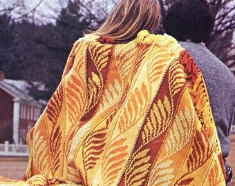 May include: A couple is wrapped in a large, colorful blanket with a leaf pattern. The blanket is made of a soft, textured fabric and features shades of yellow, orange, and brown.