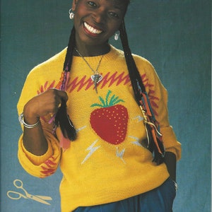 Peut inclure: Un pull jaune avec une grande fraise rouge sur le devant. Le pull présente également des motifs en zigzag roses et blancs et des éclairs. Un vêtement vintage.