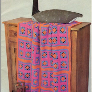 May include: A crocheted blanket with pink, orange, and blue squares, draped over a wooden cabinet with a carved goose on top.