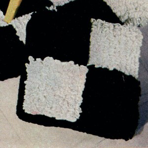 May include: Close-up of a black and white checkerboard pattern. The squares are textured, with the white squares appearing to have a fuzzy, raised surface. The black squares are smooth. The overall design is geometric and graphic.