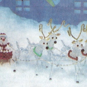 Op de afbeelding: Een feestelijke kerstversiering met de kerstman en een metgezel in een rode slee getrokken door vier rendieren. De rendieren en de slee zijn gemaakt van heldere kralen, met gouden accenten en rode en groene details.