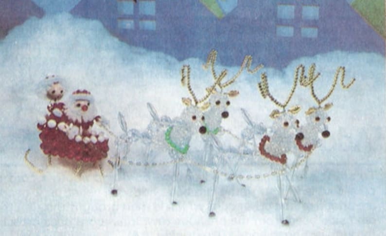 Op de afbeelding: Een feestelijke kerstversiering met de kerstman en een metgezel in een rode slee getrokken door vier rendieren. De rendieren en de slee zijn gemaakt van heldere kralen, met gouden accenten en rode en groene details.