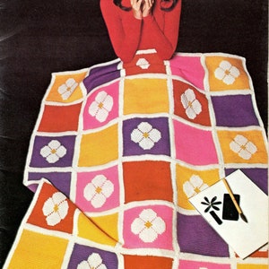 May include: A colorful crocheted afghan with a floral pattern. The afghan is made up of squares in shades of pink, purple, orange, yellow, and red. Each square features a white crocheted flower.