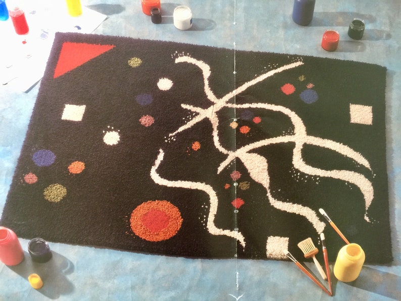 May include: A black rug with a white abstract design and colorful dots. The rug is being painted with brushes and paint.