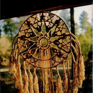 Puede incluir: Un atrapasueños artesanal con un diseño circular tejido. El centro presenta un patrón detallado y largas borlas texturizadas cuelgan de la parte inferior. El atrapasueños está hecho con fibras de color natural, creando una estética bohemia.