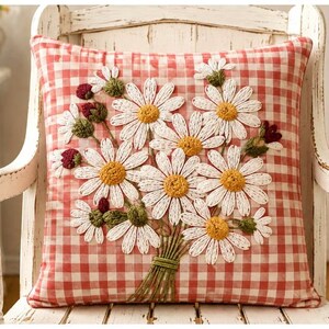 May include: A square throw pillow featuring a red and white gingham check pattern. The center displays a raised, textured embroidery of a bouquet of white daisies with yellow centers, green stems, and small dark red flower buds.