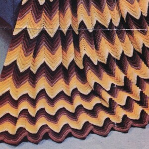 May include: A handmade crochet blanket with a chevron pattern. The blanket features a repeating zig-zag design in shades of yellow, brown, and black. The blanket is made of soft yarn and is perfect for snuggling up on the couch.