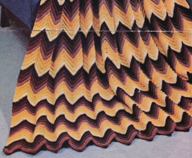 May include: A handmade crochet blanket with a chevron pattern. The blanket features a repeating zig-zag design in shades of yellow, brown, and black. The blanket is made of soft yarn and is perfect for snuggling up on the couch.