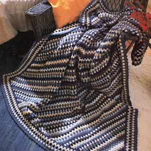 May include: A blue, beige, and white crocheted throw blanket with a textured pattern. The blanket is folded and draped over a chair.