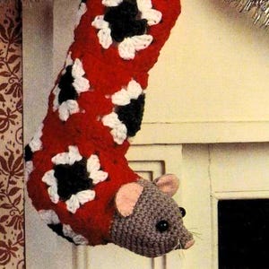 May include: A handmade Christmas stocking with a crochet mouse head. The stocking is red with white and black floral patterns. The mouse has a gray body, pink ears, and black eyes. A unique holiday decoration.