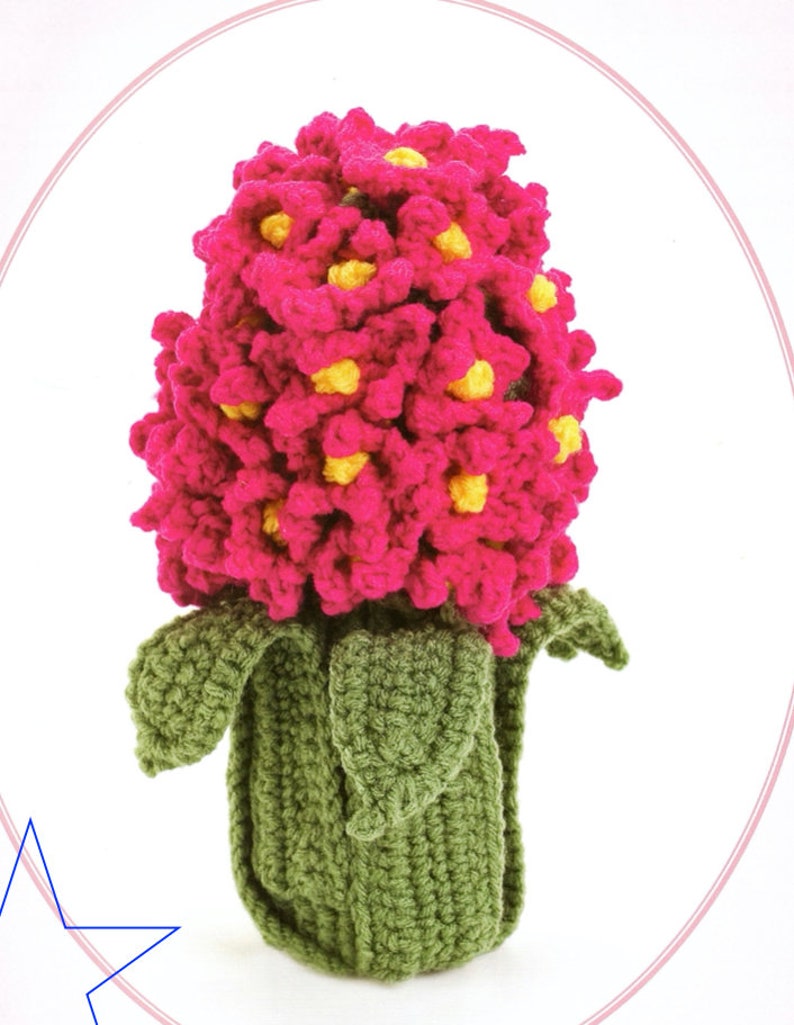 May include: A crocheted hyacinth flower with pink petals and yellow centers. The flower is in a green crocheted pot with leaves.