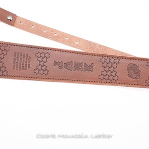 May include: Brown leather guitar strap with a star pattern and the text "JANK" embossed on it. The strap also has a quote about the forest and the words "Ozark Mountain Leather".
