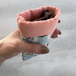 May include: A pink and blue fabric pouch with a floral pattern. The pouch is lined with a soft pink fabric and is designed to hold glasses.