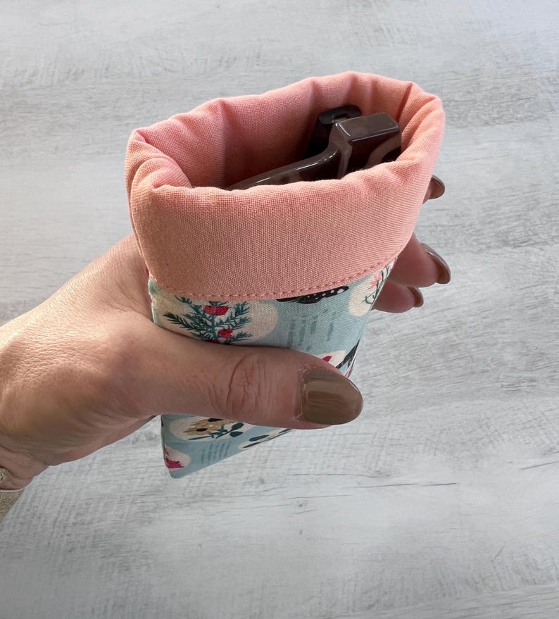 May include: A pink and blue fabric pouch with a floral pattern. The pouch is lined with a soft pink fabric and is designed to hold glasses.