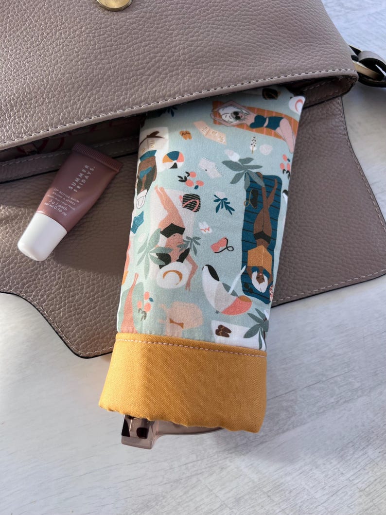 May include: A light blue and yellow fabric pouch with a colorful print of people and palm trees. The pouch is partially inside a brown leather purse.