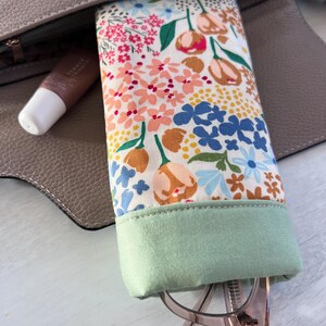 May include: A floral patterned glasses case with a green fabric lining. The case is open and a pair of glasses is inside.