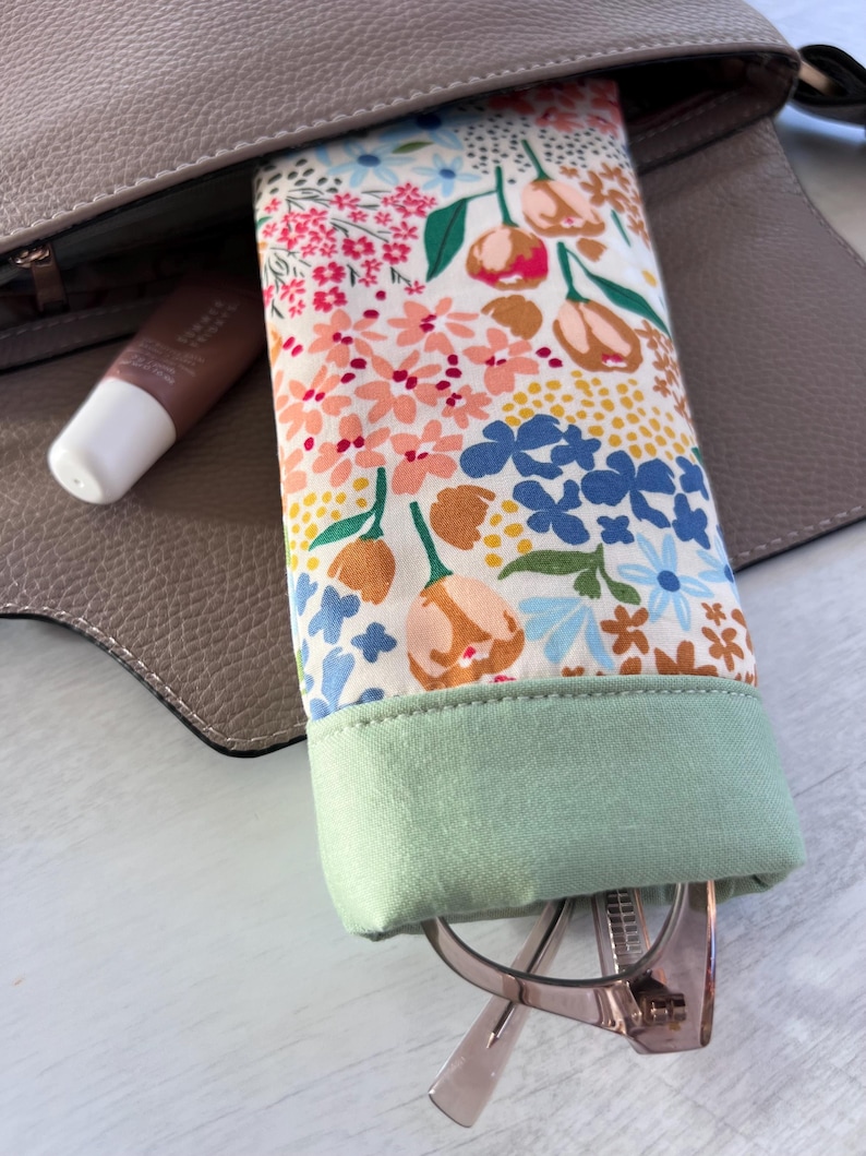 May include: A floral patterned glasses case with a green fabric lining. The case is open and a pair of glasses is inside.
