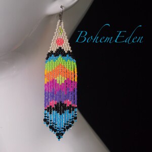 May include: A pair of long, colorful beaded earrings with a white, black, and pink geometric design at the top. The earrings are made with small, colorful beads and have a fringe-like appearance.
