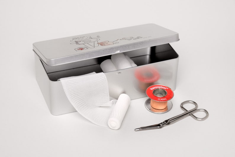 May include: A silver metal first aid kit with a cartoon illustration on the lid. The kit is open and contains bandages, gauze, a roll of adhesive tape, and a pair of scissors.