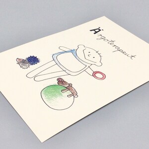 May include: A hand-drawn illustration of a person with a red ring, a blue shirt, and a green ball. The person is holding a teddy bear. The illustration is on a white card with the text "A'rgoterapeut" written in black.