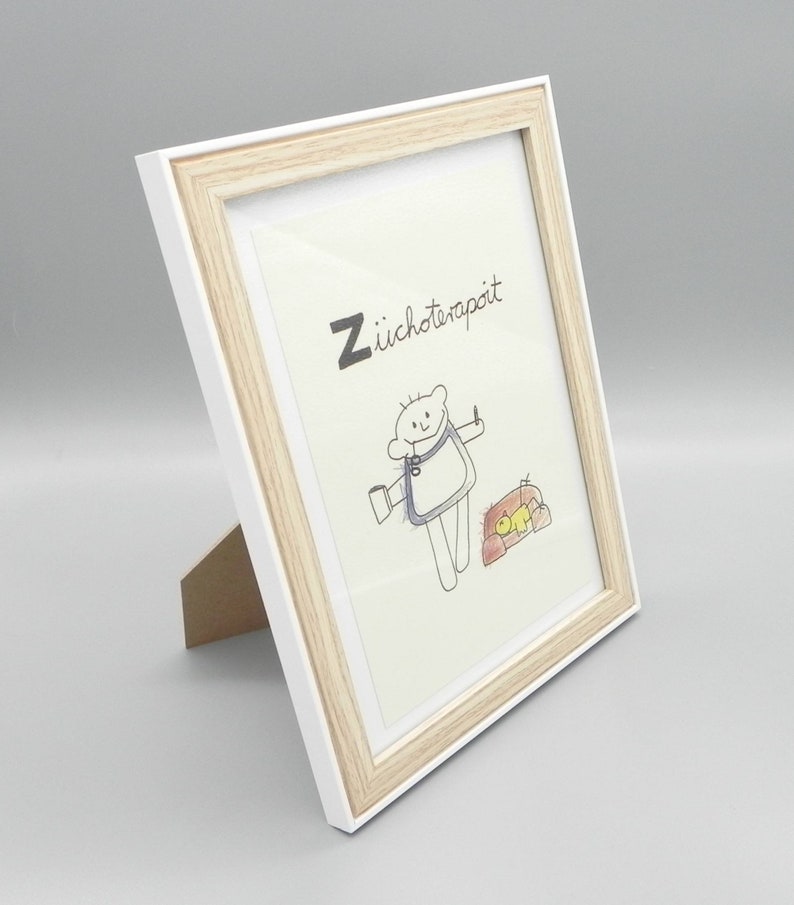 May include: A white picture frame with a light wood trim. The frame is standing upright on a white surface. The frame contains a drawing of a person with a cup and a small animal. The drawing is titled "Z&uuml;choterapit".