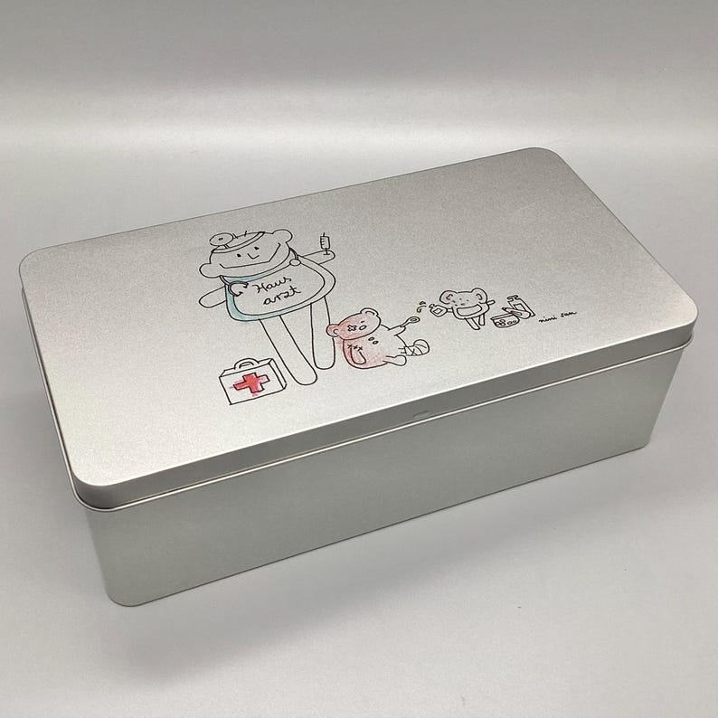 Rechteckige Metalldose als Erste Hilfe Kasten mit Schwingdeckel.
Auf dem Deckel eine kindliche Illustration.nini san Junge als Hausarzt mit Arzt Koffer, kranken Bär und kleiner Maus, die Medikamente vergibt.