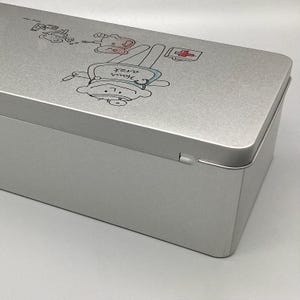 May include: A silver metal first aid kit with a cartoon illustration of a bear wearing a doctor's hat and holding a syringe. The text "your own nurse" is written on the bear's shirt.
