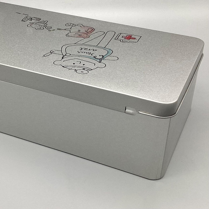 May include: A silver metal first aid kit with a cartoon illustration of a bear wearing a doctor's hat and holding a syringe. The text "your own nurse" is written on the bear's shirt.
