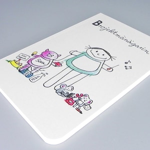 Op de afbeelding: Een wit notitieboekje met een handgetekend plaatje van een persoon met een groen shirt en een varken met een schort. De tekst "Projektmanagerin" staat op de voorkant van het notitieboekje.