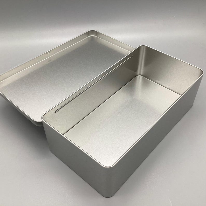 May include: A silver metal rectangular box with a hinged lid. The box is open and the inside is visible.