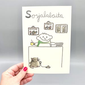 Peut inclure: Une carte de v&oelig;ux blanche avec une illustration dessin&eacute;e &agrave; la main repr&eacute;sentant une personne assise &agrave; un bureau avec une tasse de caf&eacute;, un chat et une souris. Le texte 'Sosjalabaita' figure en haut, avec des dessins encadr&eacute;s sur le mur.
