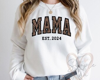 May include: White sweatshirt with a black and leopard print "MAMA EST. 2024" graphic.