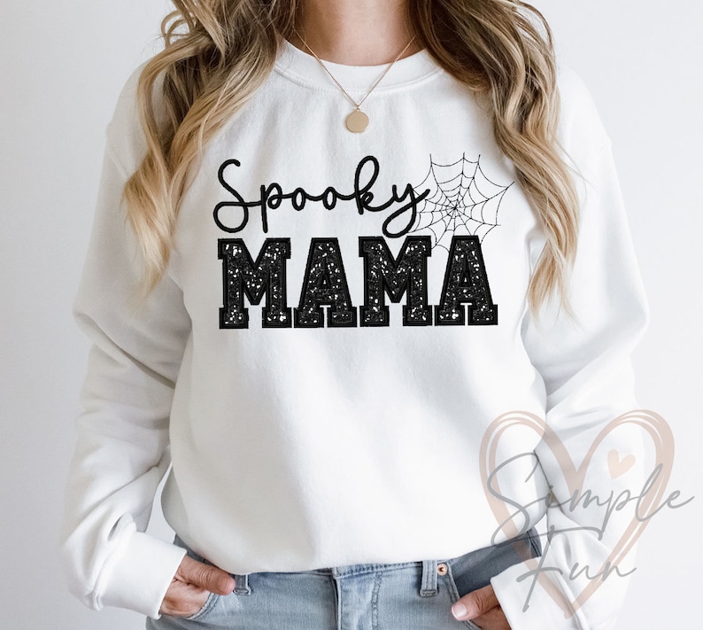 May include: White sweatshirt with black text that reads "Spooky Mama" with a black spiderweb graphic above the text.