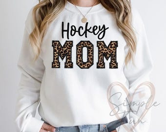 May include: White sweatshirt with the text "Hockey Mom" in black lettering with a leopard print design.