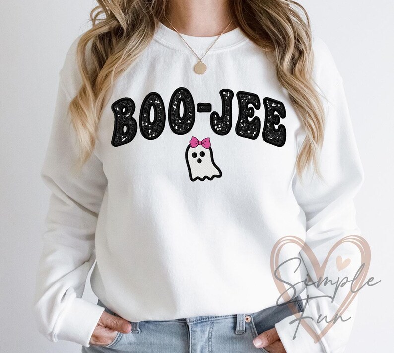 May include: White sweatshirt with the text "BOO-JEE" in black, outlined in white, above a cartoon ghost with a pink bow. The sweatshirt is a crew neck style.