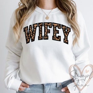 May include: White sweatshirt with the word "WIFEY" printed in black with a leopard print pattern.