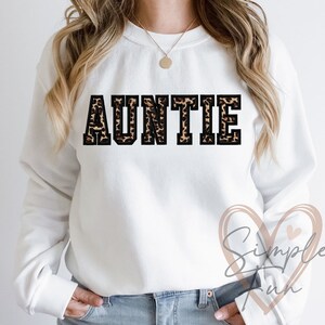 May include: White sweatshirt with the word "AUNTIE" printed in black with a leopard print pattern.