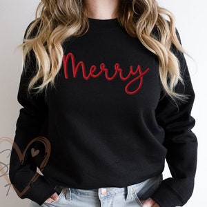 Pu&ograve; includere: Felpa nera con la parola "Merry" in lettere corsive rosse.