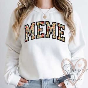 May include: White sweatshirt with a floral print design that spells out the word "MEME" in black block letters.