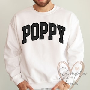 May include: White sweatshirt with the word "POPPY" printed in black block letters.