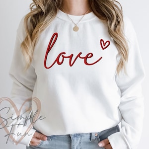 May include: White sweatshirt with the word "love" in red cursive lettering and a small red heart.
