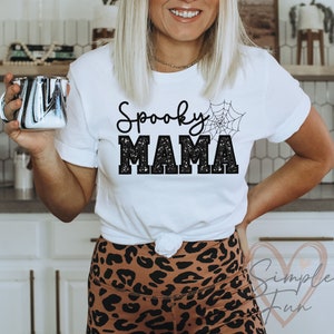May include: White t-shirt with black glitter text that reads "Spooky Mama" and a black spiderweb graphic.