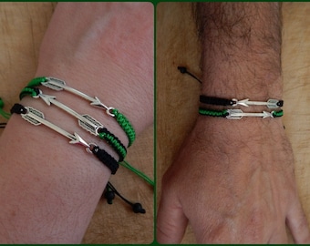 May include: Two bracelets with black and green cords and silver arrow charms. The bracelets are worn on a person's wrist.