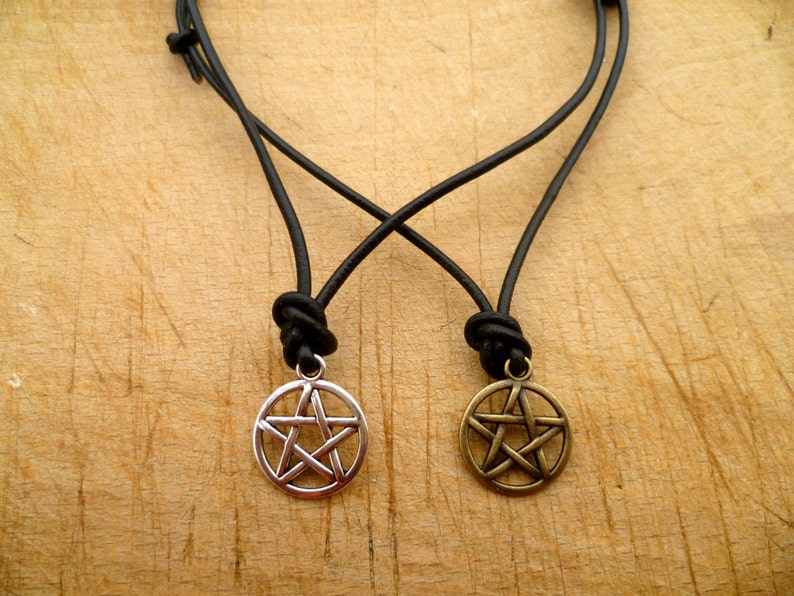 May include: Two leather necklaces with pentagram pendants. One pendant is silver and the other is gold.