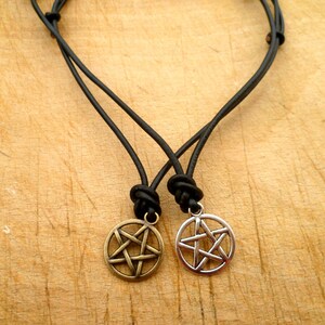 May include: Two black leather cord necklaces with silver and bronze pentagram pendants.
