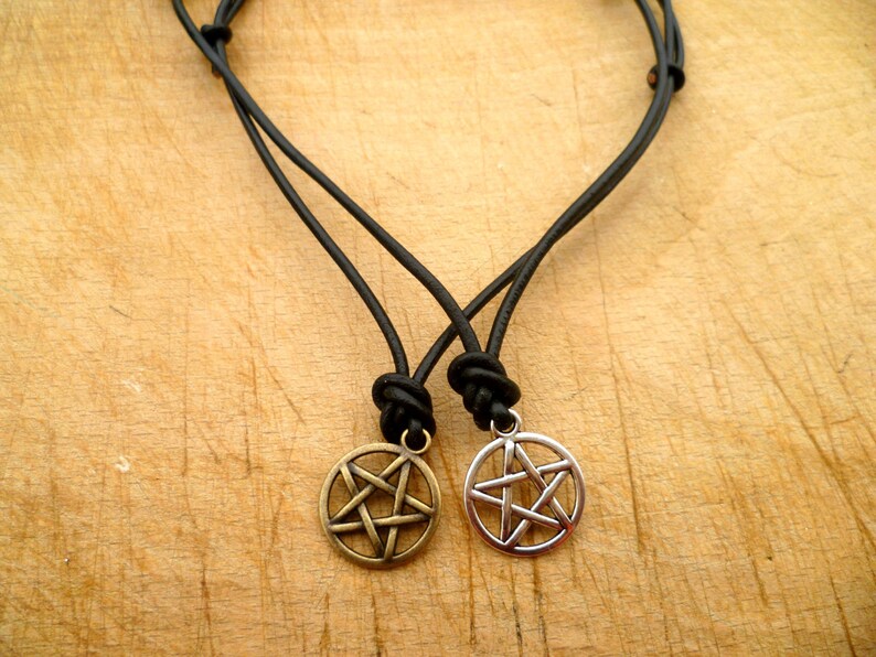 May include: Two black leather cord necklaces with silver and bronze pentagram pendants.