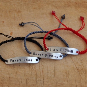 May include: Three braided bracelets with adjustable closures and metal tags with the words "Worry less", "Never give up", and "I am ENOUGH".