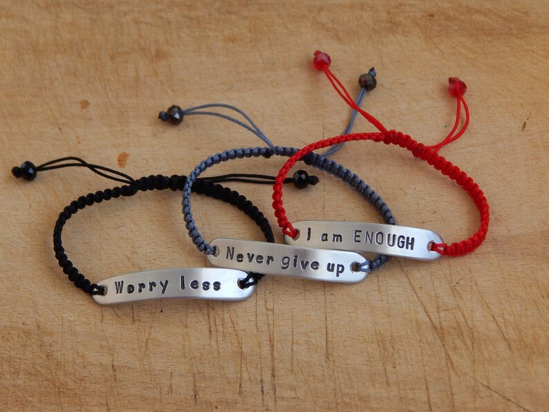 May include: Three braided bracelets with adjustable closures and metal tags with the words "Worry less", "Never give up", and "I am ENOUGH".