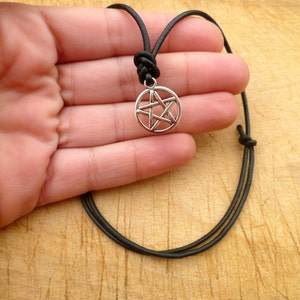 May include: A silver pentagram pendant necklace on a black leather cord. The pendant is a five-pointed star within a circle.