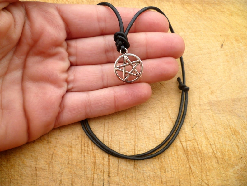 May include: A silver pentagram pendant necklace on a black leather cord. The pendant is a five-pointed star within a circle.
